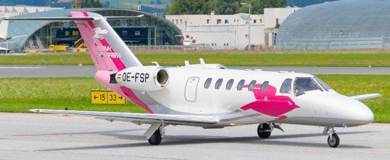 A white and pink Cessna Citation CJ4 with registration OE-FSP on the tarmac.