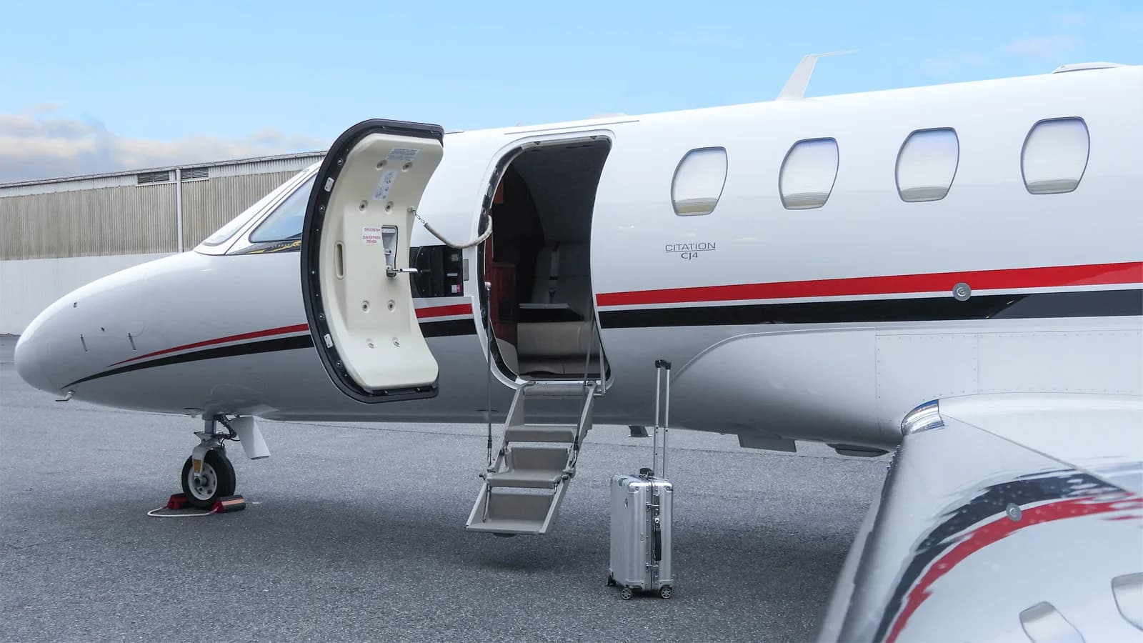 A close-up view of the open main cabin door and forward fuselage of a white Citation CJ4 business jet, showing "CITATION CJ4" text and a suitcase.