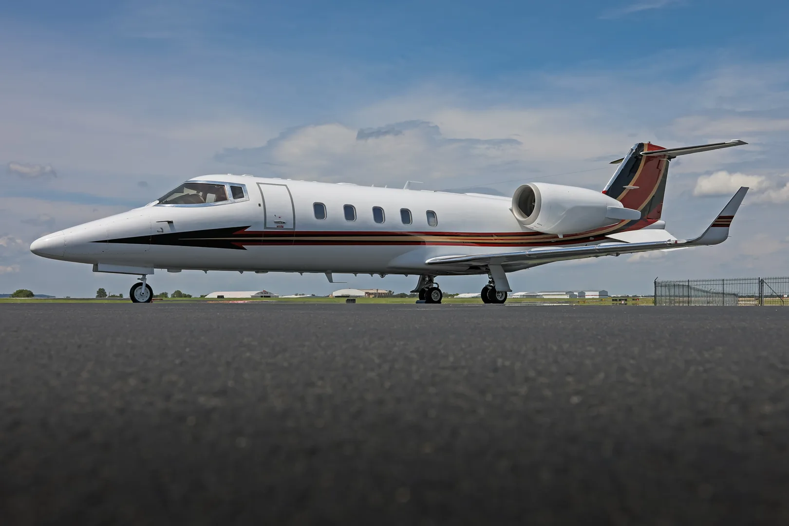 A white business jet with red and black tail accents parked on an asphalt runway, viewed from a low angle.