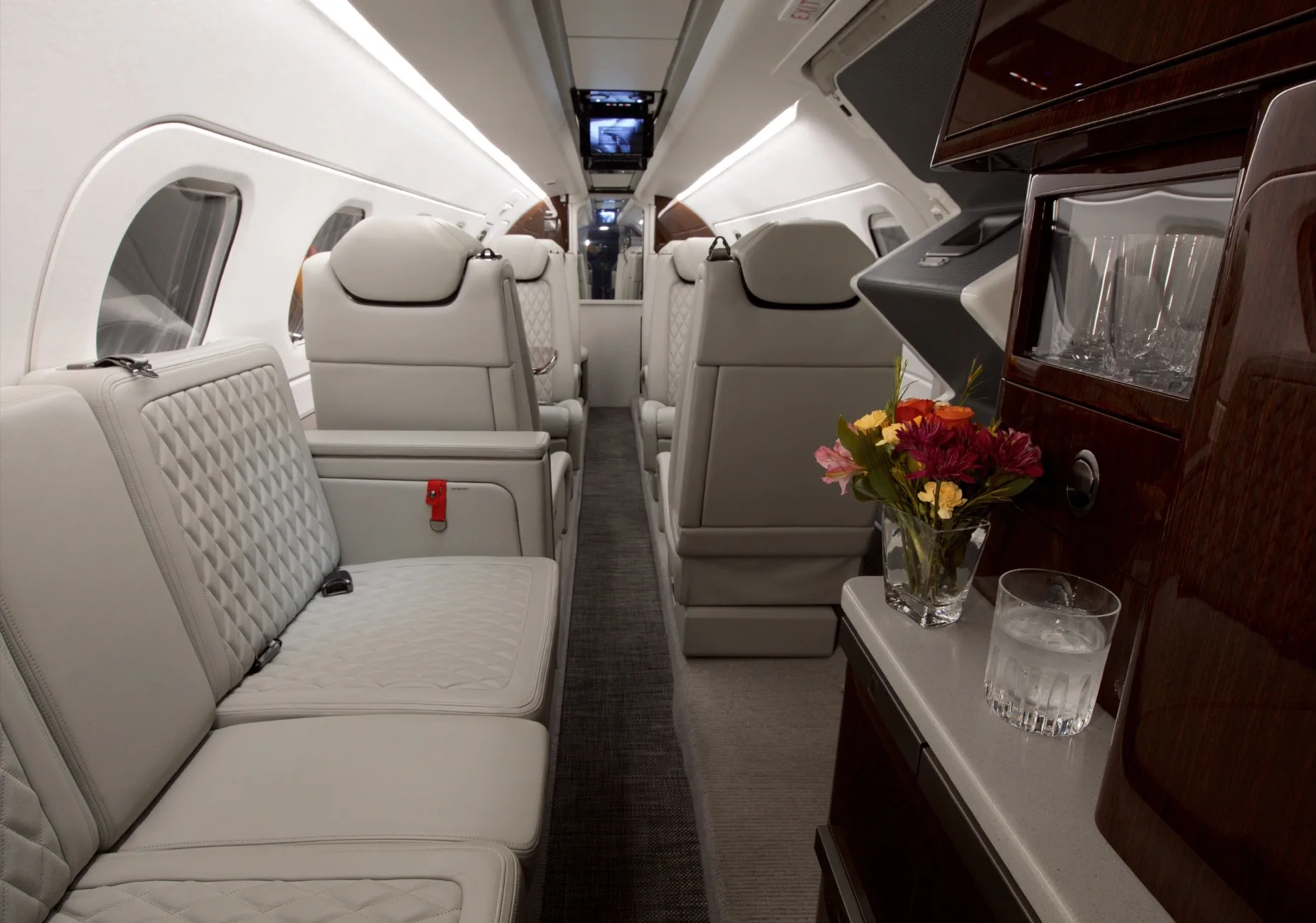 A wide view of the Embraer Phenom 300E cabin interior, showing light-colored seating, dark wood accents, and a floral arrangement.