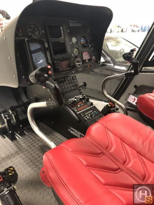 View of the helicopter cockpit with red seats and instrument panel.