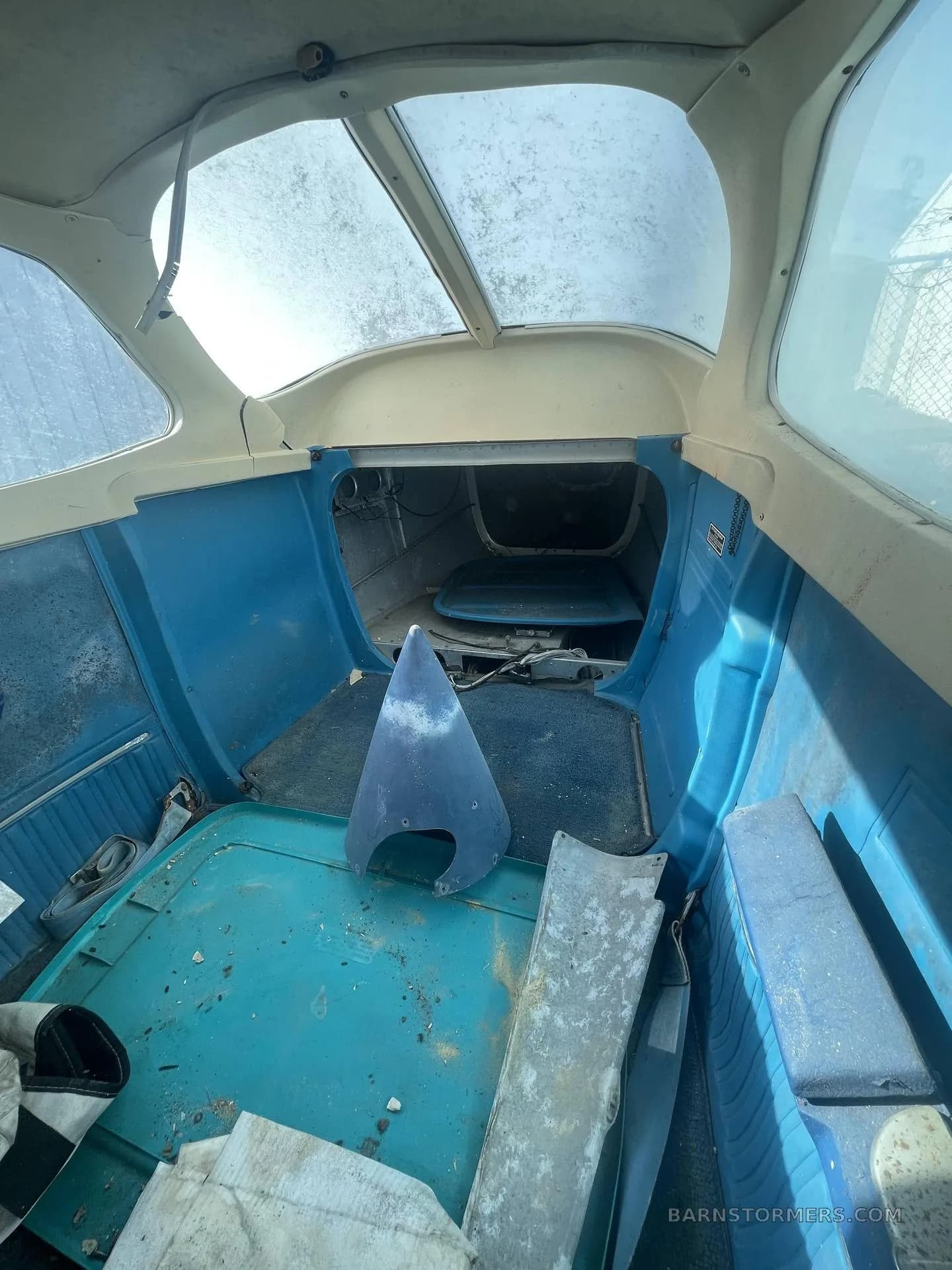 The stripped and weathered interior cabin of a light aircraft, showing blue side panels and a clear rear window.