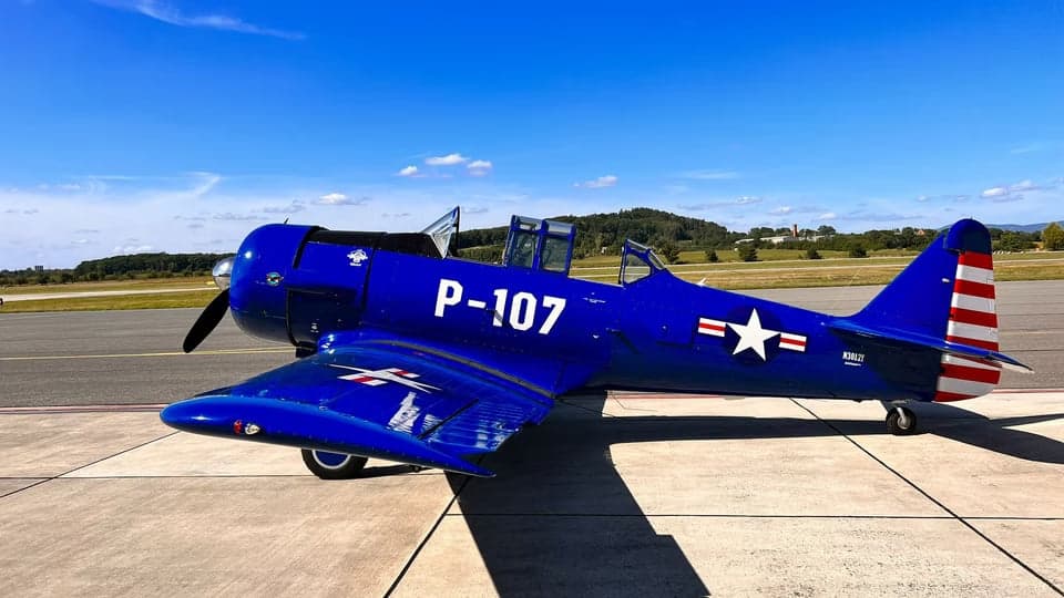 A blue North American Aviation T-6 Texan aircraft parked on the tarmac with a white star and red and white stripes on the tail.