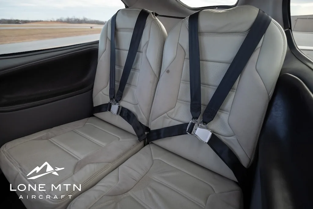 Two light-colored leather rear seats with black seatbelts inside the aircraft cabin.
