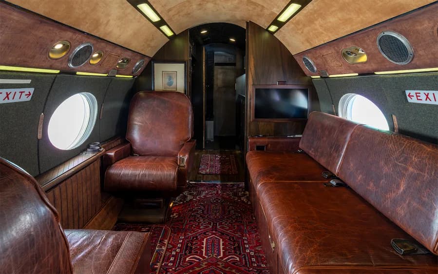 Aircraft interior with leather seats, a couch, and a patterned rug.