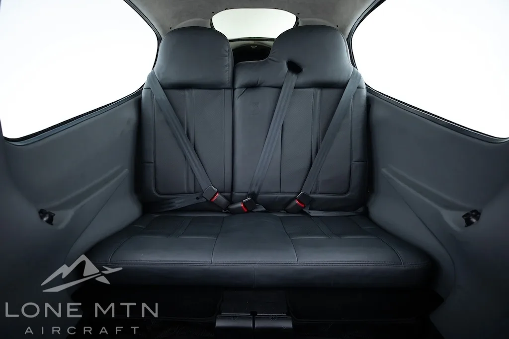A wider view of the black leather rear seats of a Cirrus SR22 aircraft cabin with seatbelts fastened.