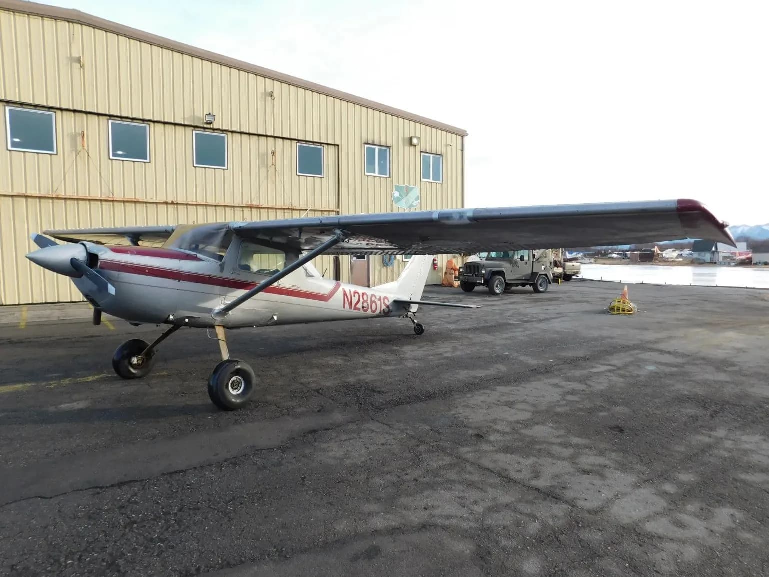 A silver and red single-engine propeller aircraft (N2861S) parked on a tarmac with a building and vehicles in the background.