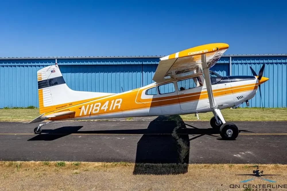 A side profile view of a white and orange Cessna 185 Skywagon (N1841R) with 'Cessna' on its orange wing.