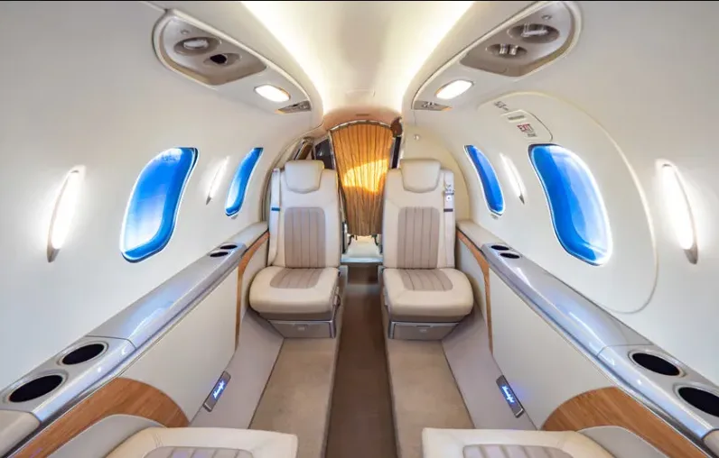 A view down the aisle of a HondaJet Elite's cabin, showing beige leather seats, wood trim, and a closed privacy curtain at the rear.