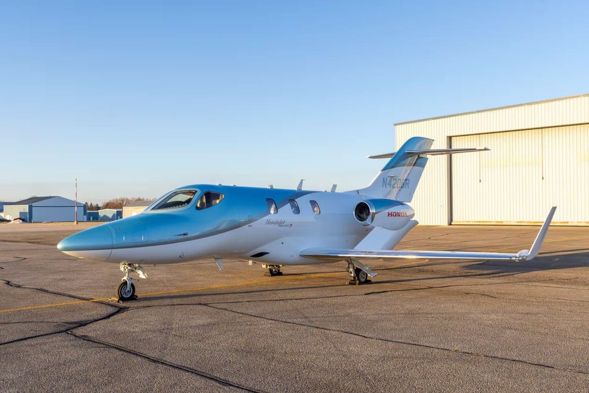 A HondaJet Elite S aircraft with a blue and white paint scheme is parked on the tarmac in front of a hangar.