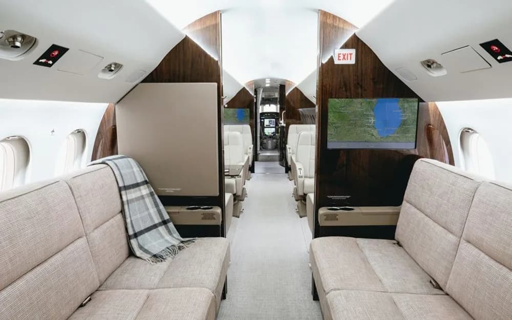 A view down the cabin of a Dassault Falcon 900EX, showing beige fabric divans in the foreground and individual leather seats further back.