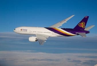 A Thai Airways Boeing 777 in flight against a blue sky.