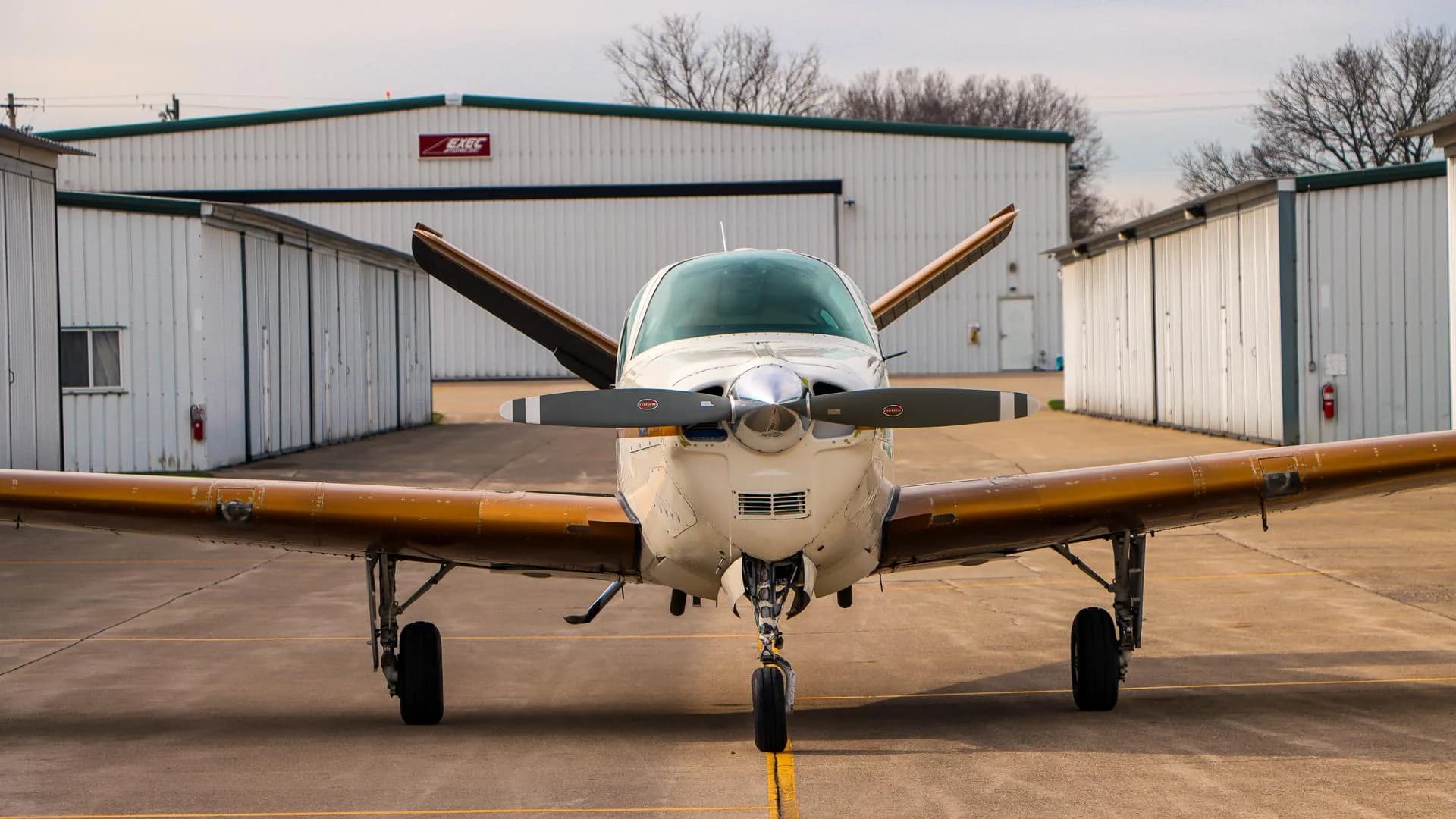Close-up front view of a white and gold Beechcraft Bonanza with its propeller blades angled.