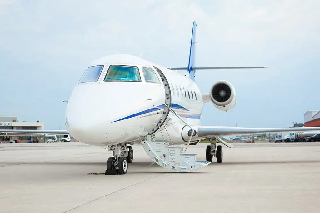 A white business jet with blue stripes and tail, parked on an airport tarmac with its main entry door open and stairs extended.