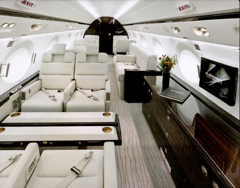 View of the interior cabin with white seats, a table set for dining, and a bottle of wine.