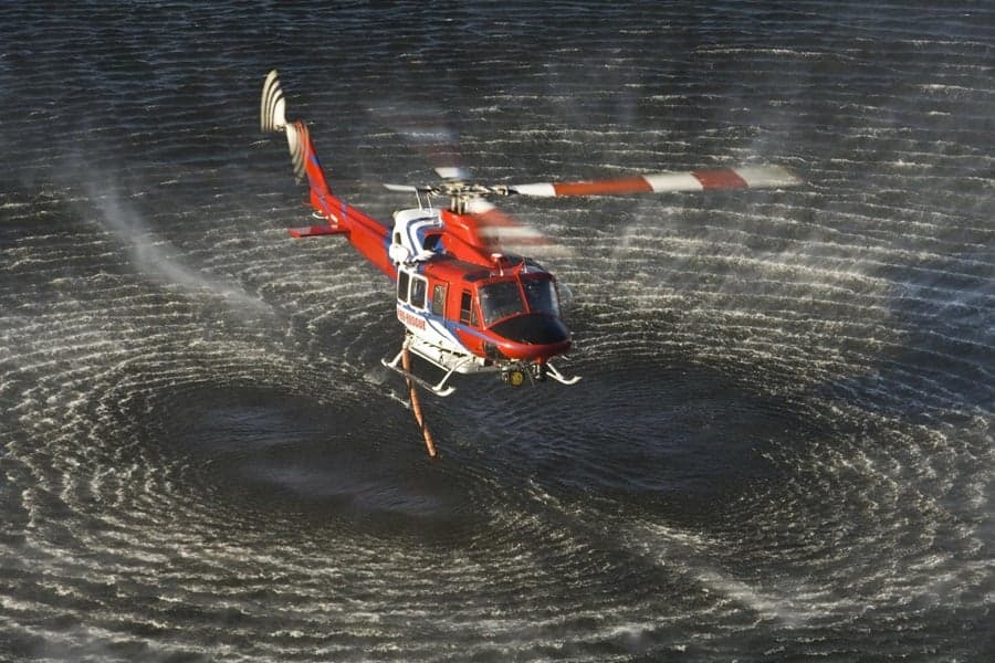 Red and white helicopter flying over water.
