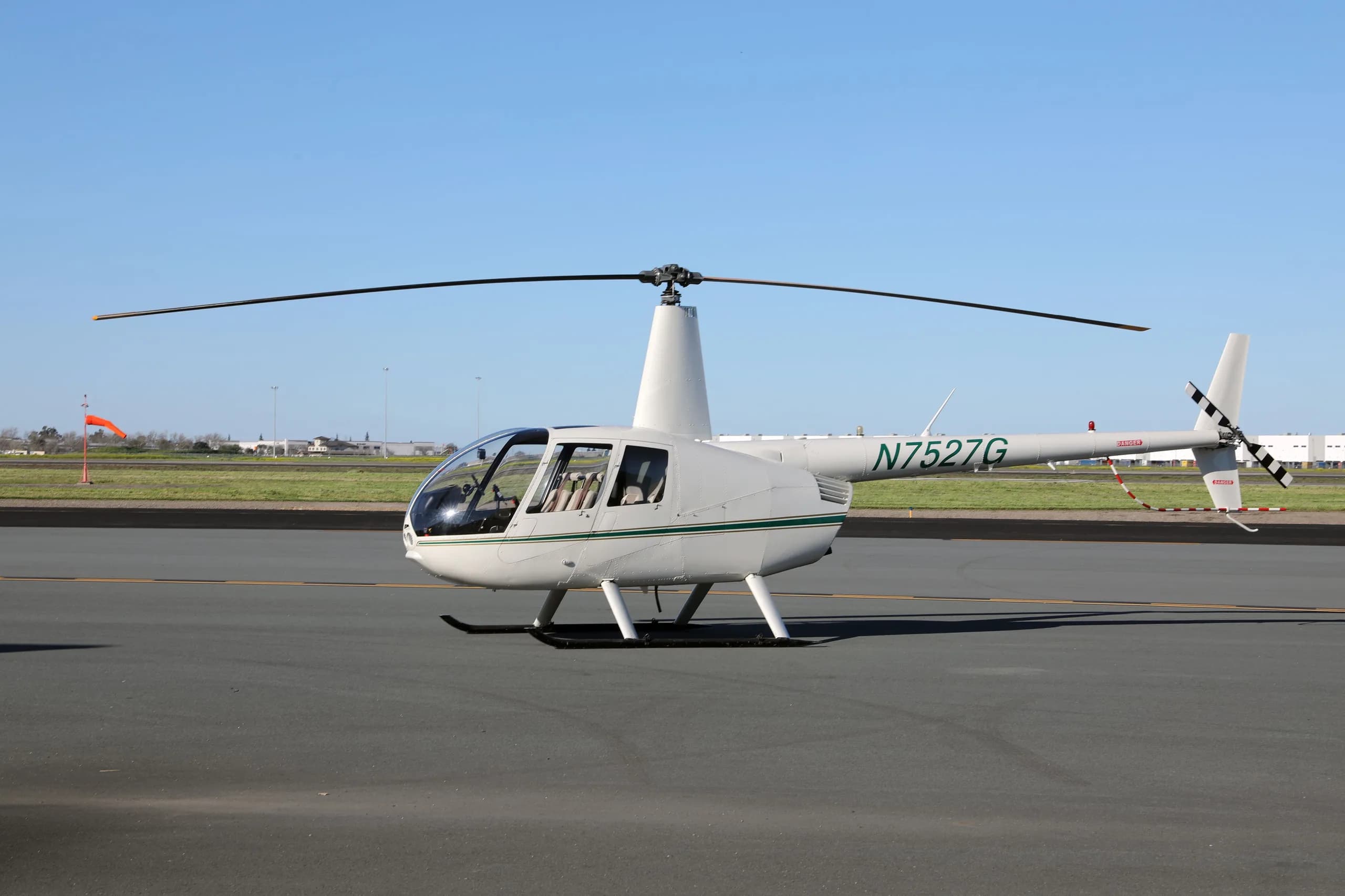 White Robinson R44 Raven II helicopter with a green stripe, registration N7527G, parked on an airfield.