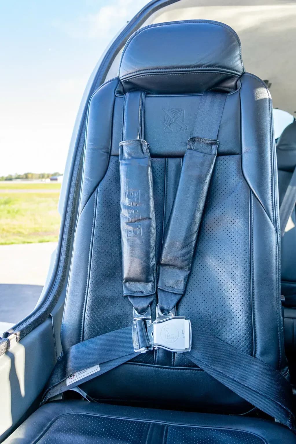 A close-up view of a black leather aircraft seat with a five-point harness.