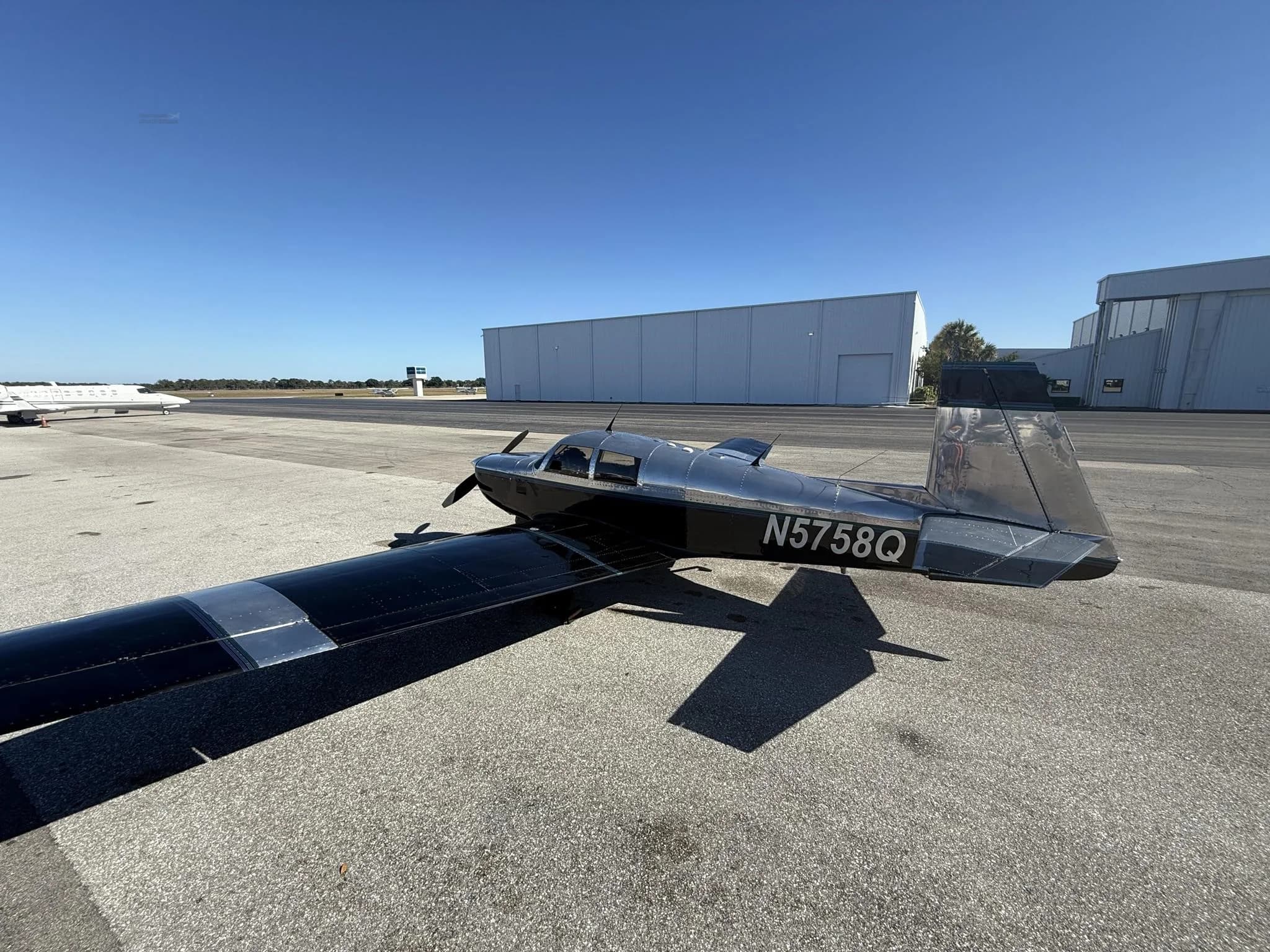 A black and silver Mooney M20 aircraft, N5758Q, parked on an asphalt tarmac under a clear blue sky.