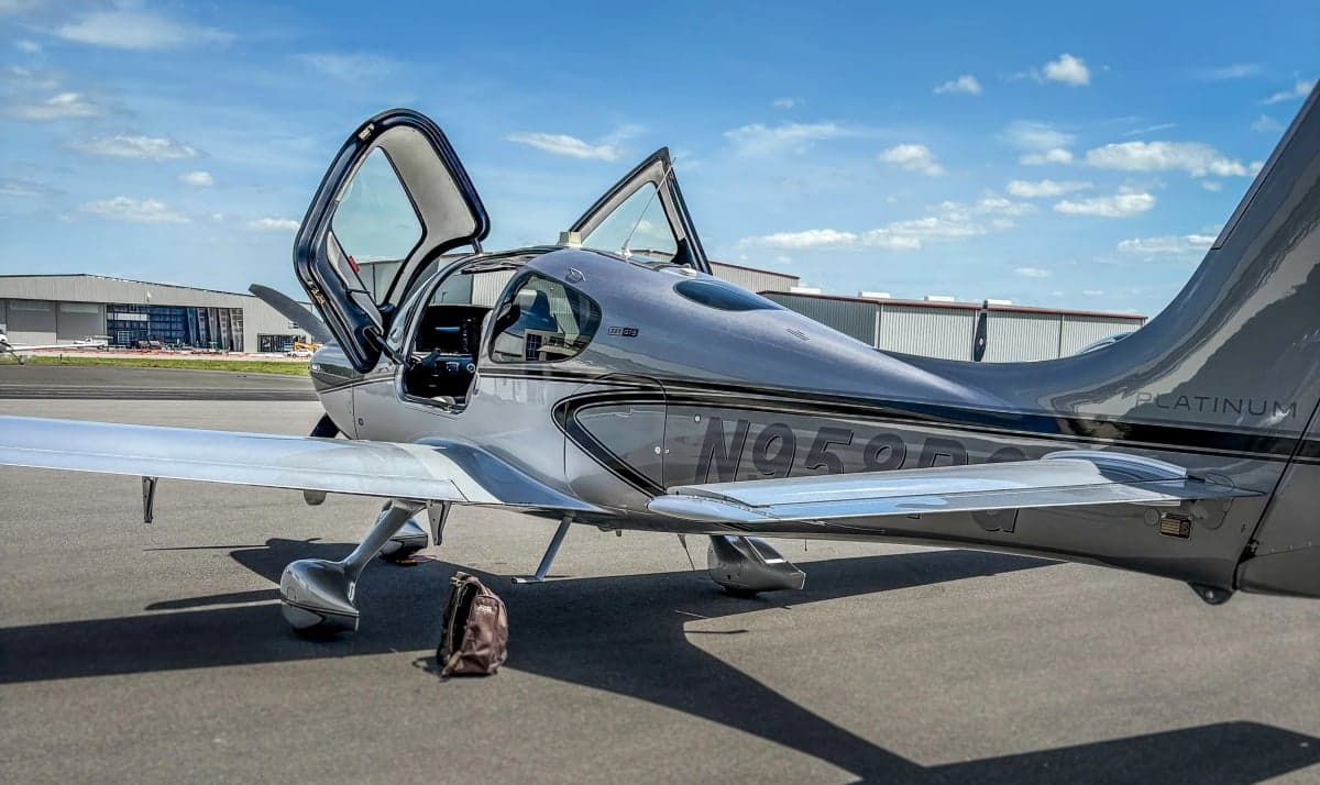 A Cirrus SR22T aircraft is parked on the tarmac with its gull-wing doors open.