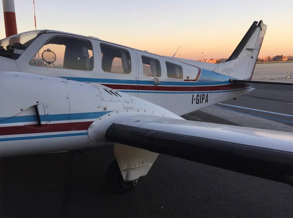 A white twin-engine aircraft with blue and red stripes on the tail and fuselage, registration I-GIPA, parked on an airfield at sunset.
