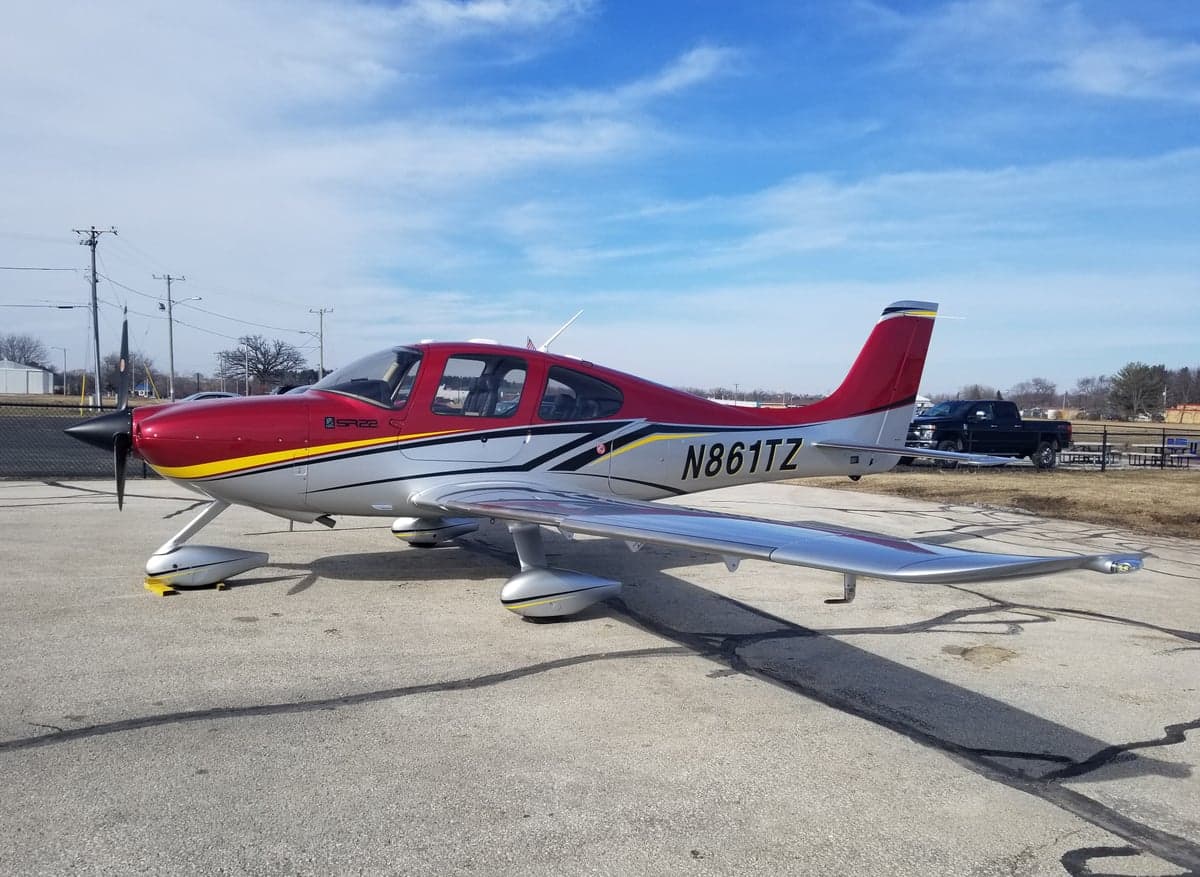 A Cirrus SR22 aircraft with a red and silver paint scheme is parked on the tarmac.