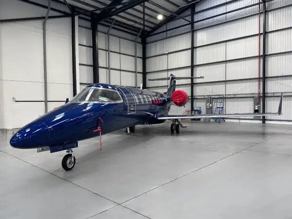 A dark blue Learjet is parked inside a hangar.