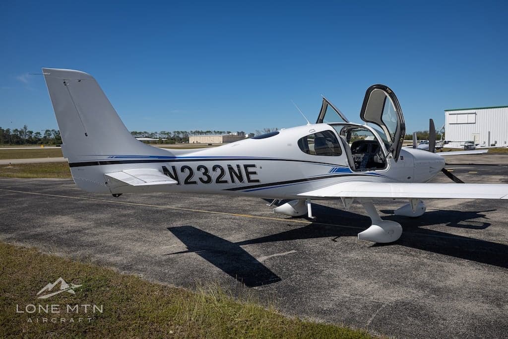 Cirrus SR22T aircraft N232NE parked on the tarmac with open doors, side view.