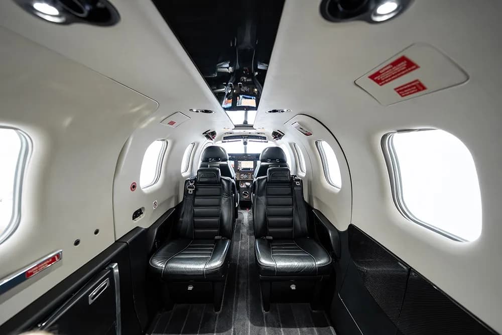 A view looking forward into the TBM 930 cabin with black leather seats and white interior panels.