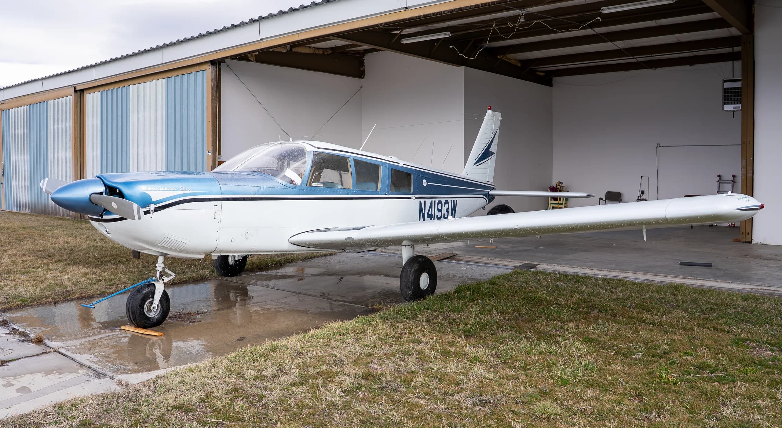 Front-side view of a white and blue single-engine propeller aircraft N4193W parked partially in a hangar.