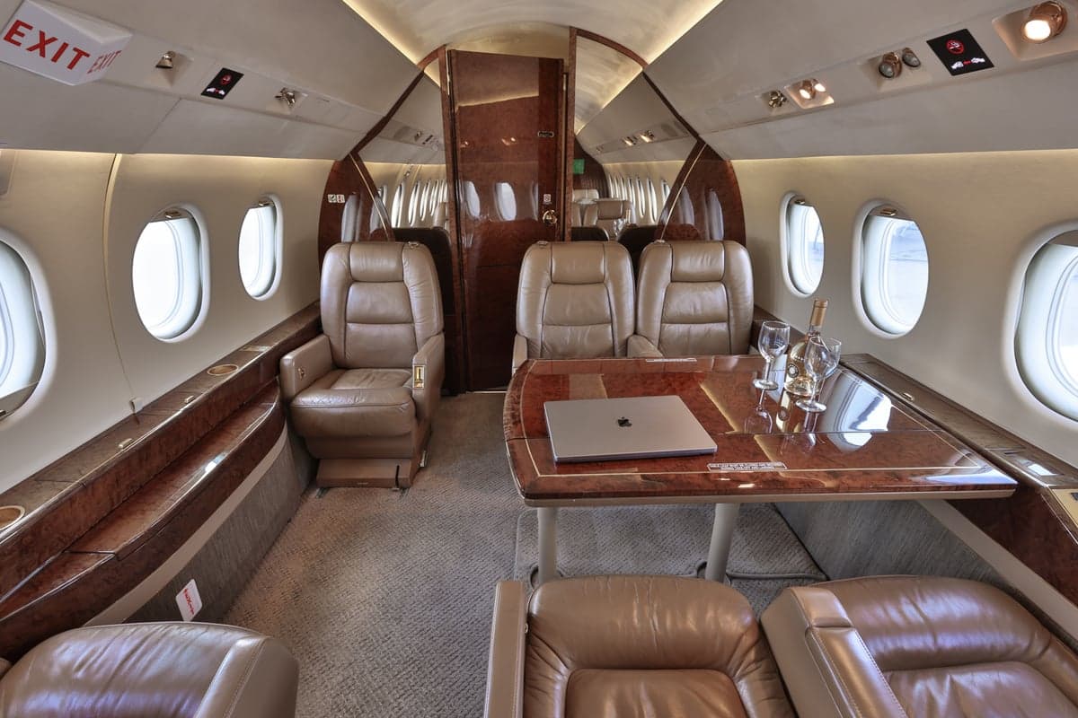 View of the aircraft interior with leather seats and a table with a laptop and wine glasses.
