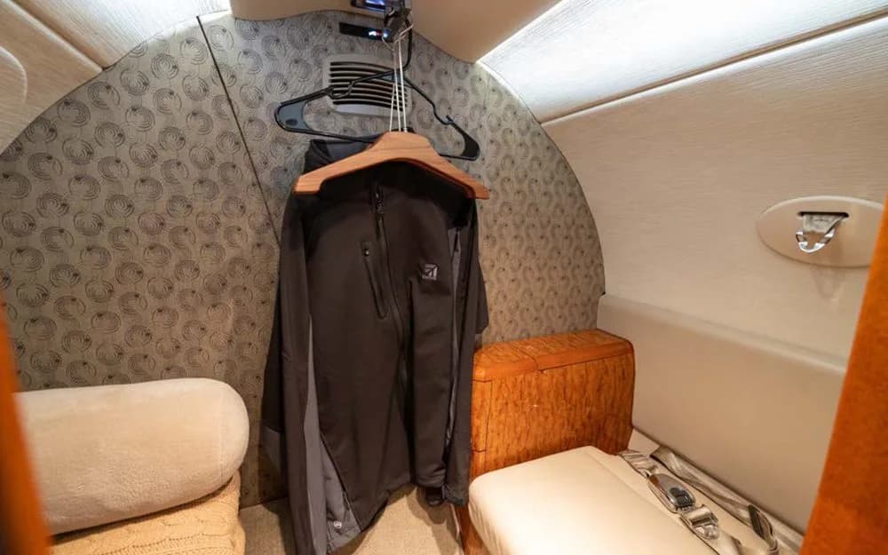 A small closet area inside a private jet cabin with a black jacket hanging on a wooden hanger.