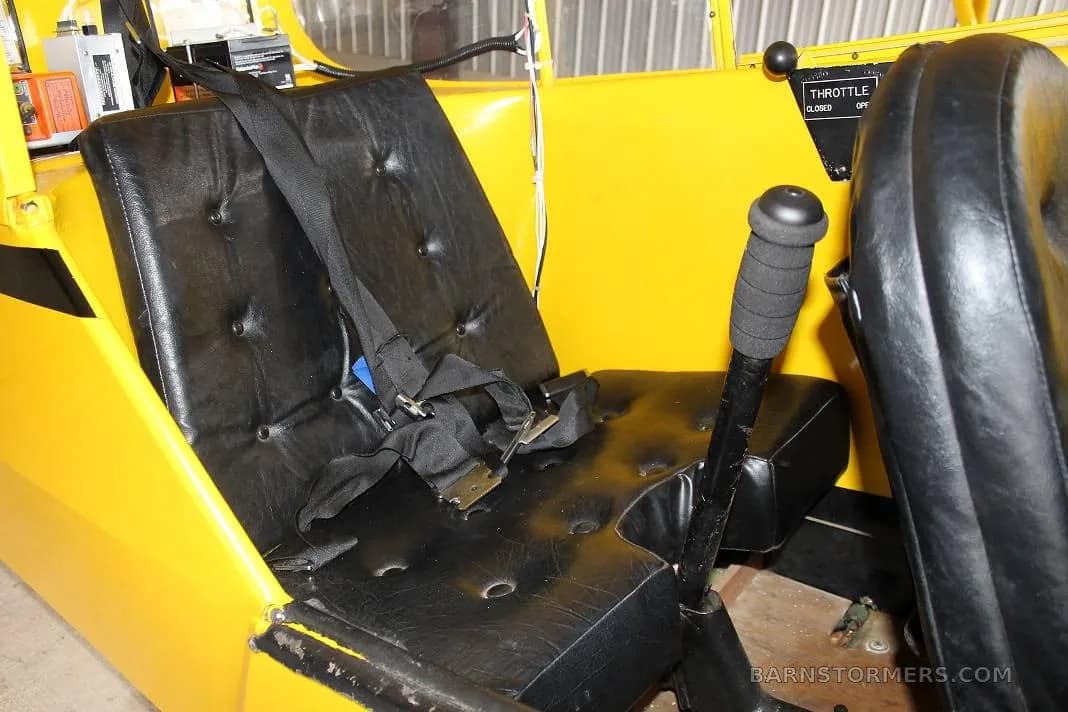 The black leather seats and control stick inside the yellow cabin of a small aircraft.
