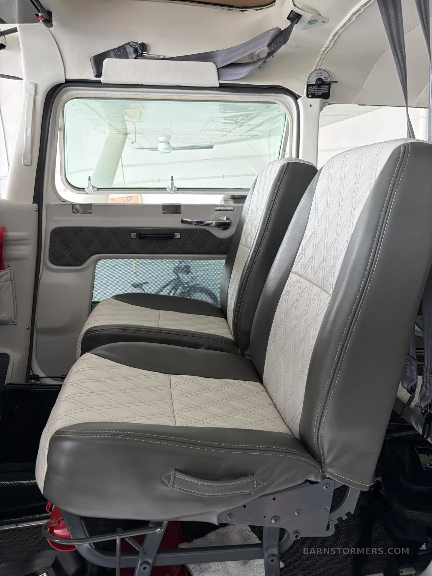 The aircraft's interior cabin, showing two rows of gray and white quilted seats with a view out the window.