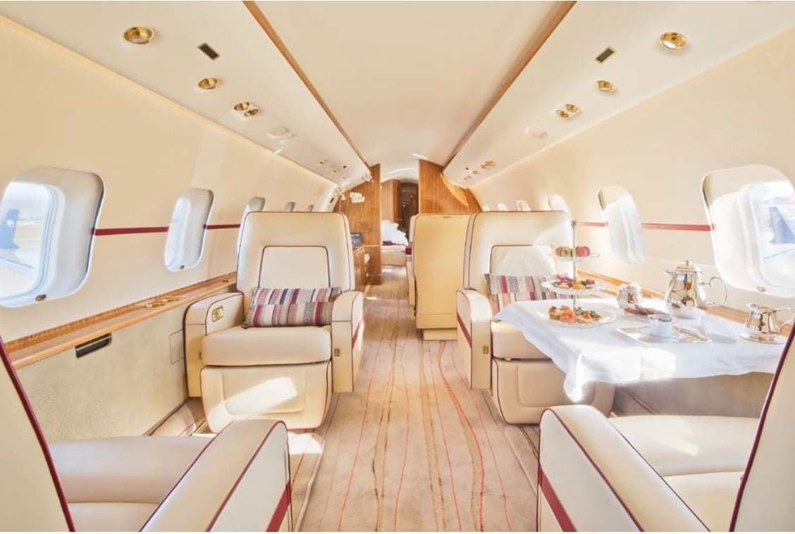 View of the aircraft's interior with cream-colored seats and a table set with refreshments.