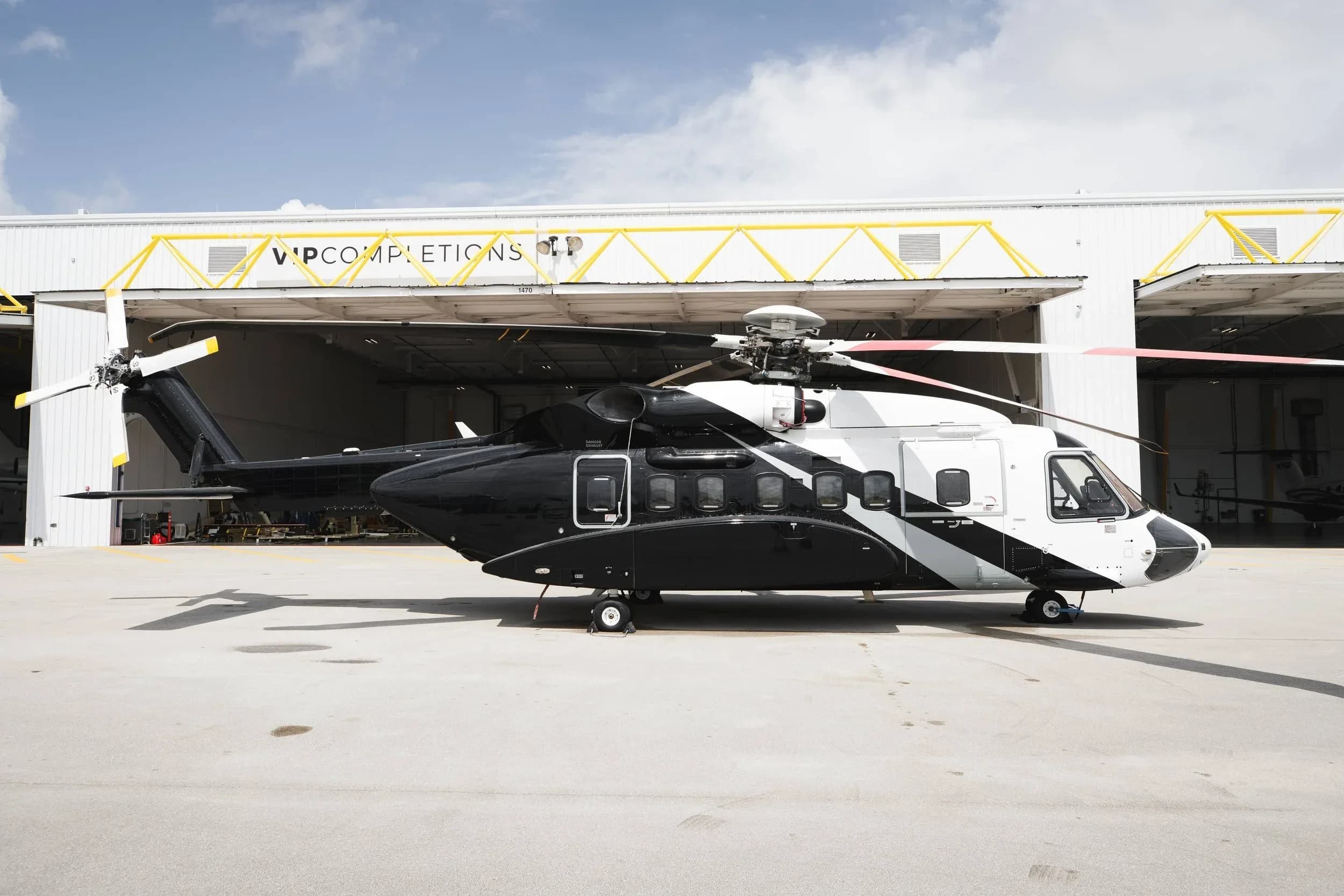 Side view of a black and white helicopter parked in front of a hangar.