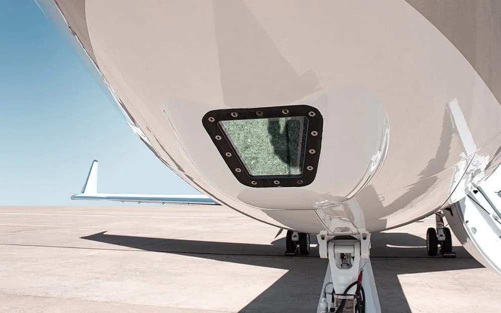 A close-up view of the underside of a white private jet, showing a small window and landing gear on an airfield.