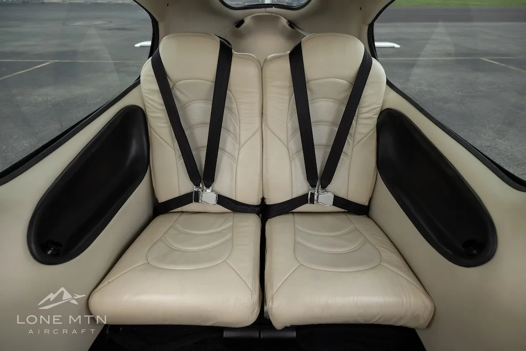 Two beige leather rear seats with black seatbelts in the aircraft cabin.