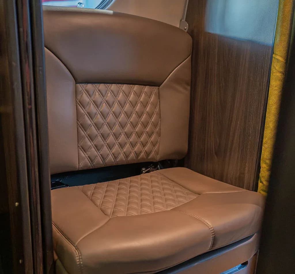 A close-up of a brown quilted leather aircraft seat with wooden paneling beside it.