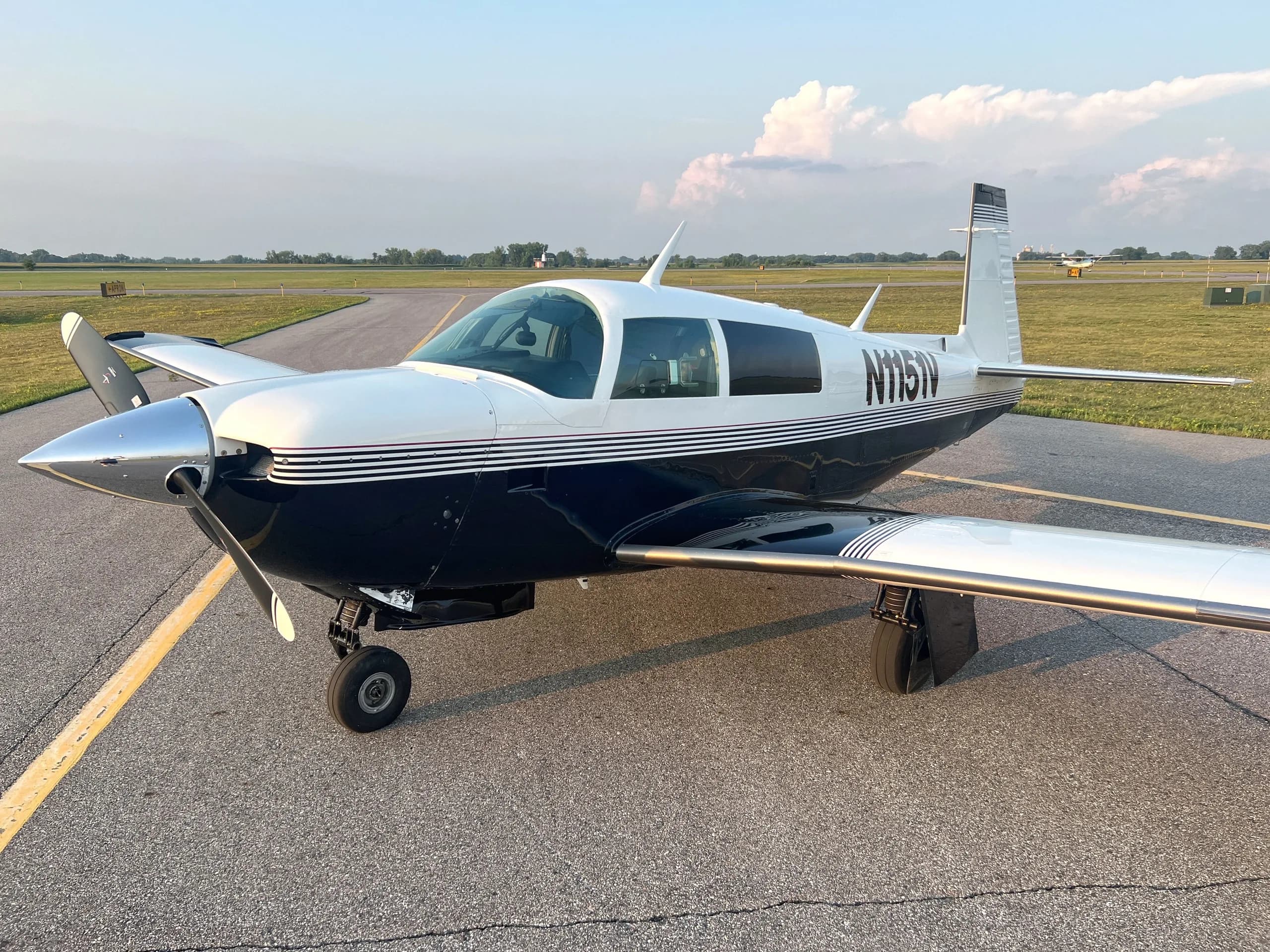 A front-side view of a white and dark blue single-engine aircraft, N1151V, on an airfield.