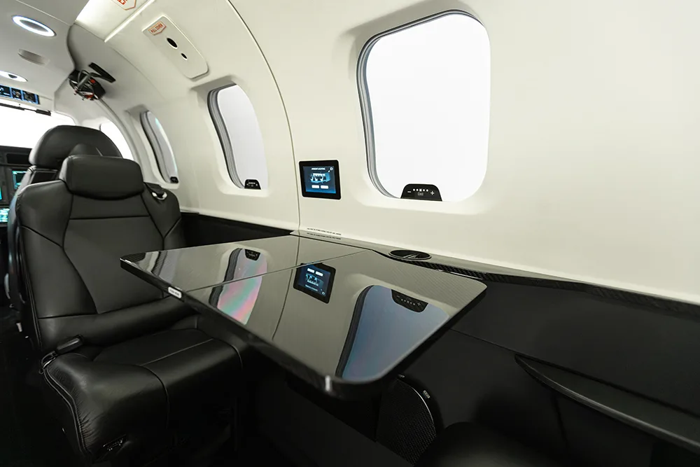A black reflective table extended between two black leather seats in a private jet cabin.