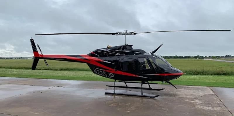 Bell 206L-4 helicopter, registration N235JP, parked on a concrete pad with a black and red paint scheme.