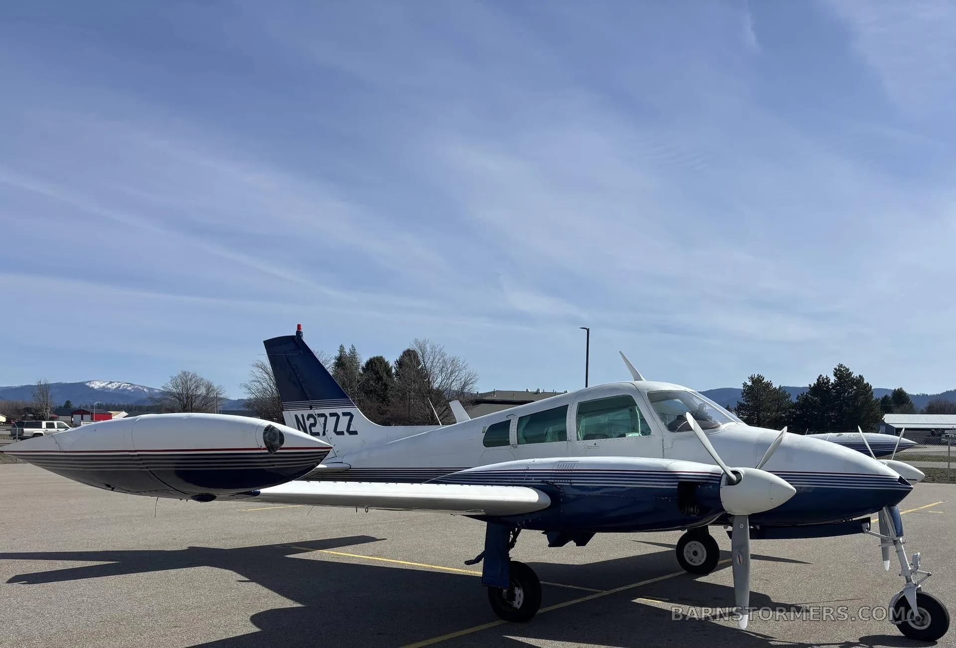 A white and blue Cessna 310I, registration N27ZZ, parked on an airfield with mountains in the background.