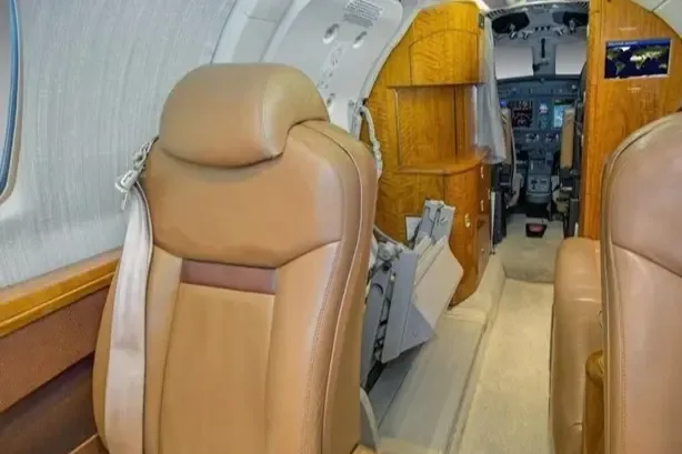 View from the aircraft cabin looking forward, showing tan leather seats and a glimpse of the cockpit.