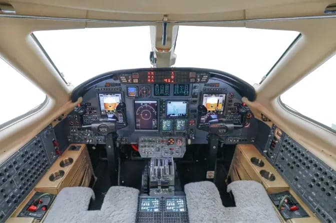 The cockpit of a business jet, showing a modern glass panel with multiple displays and controls.