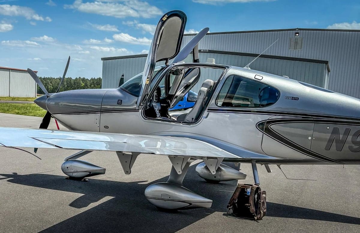 A Cirrus SR22T aircraft is parked on the tarmac with its gull-wing doors open.