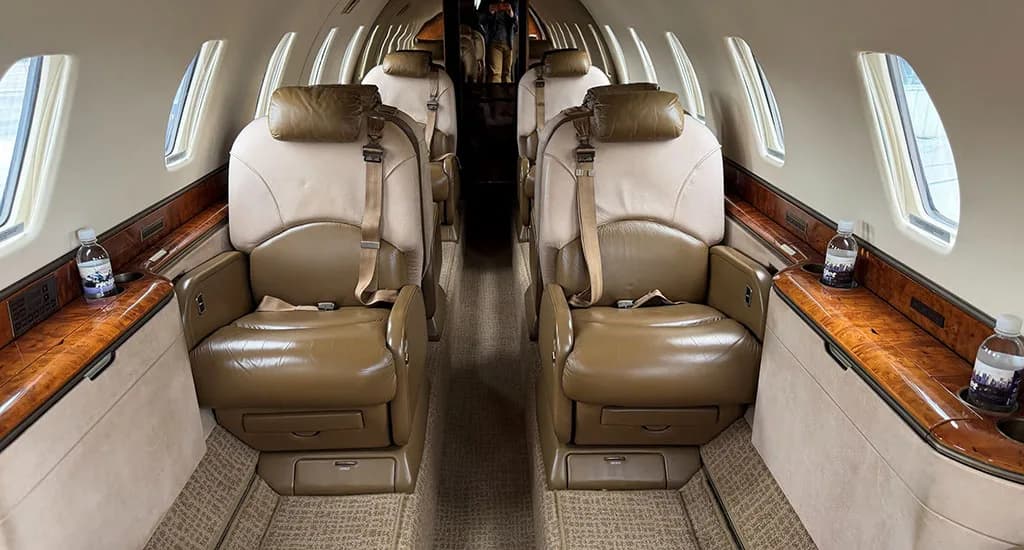 The luxurious interior cabin of a business jet, featuring two rows of tan and brown leather seats facing each other.