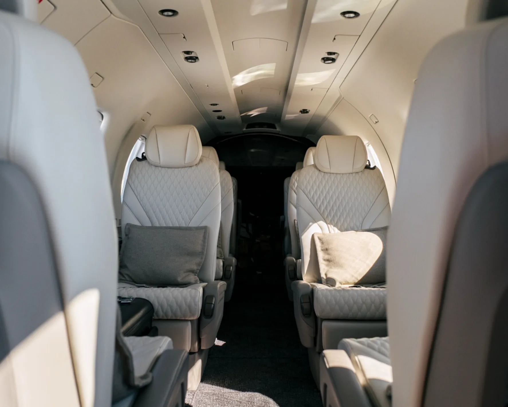 The luxurious interior cabin of an aircraft with light-colored quilted leather seats and grey pillows.