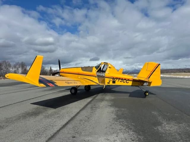Side view of a yellow crop duster aircraft with registration N773CC and black and red stripes on an airfield.