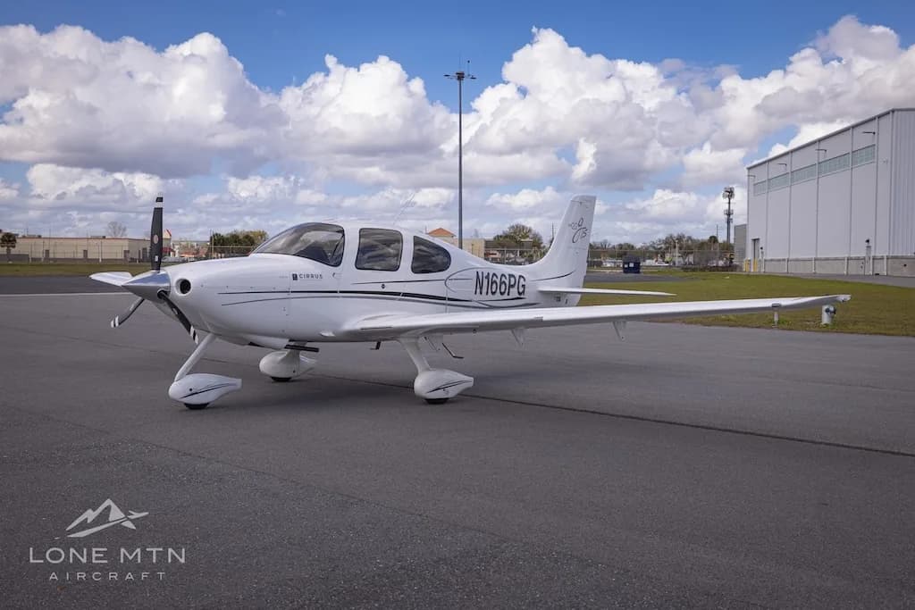 A side view of the white Cirrus SR20 aircraft (N166PG) parked on an airport tarmac.